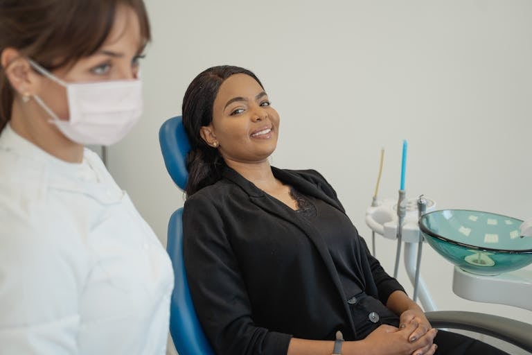 Smiling patient in a dental chair with healthcare professional nearby.